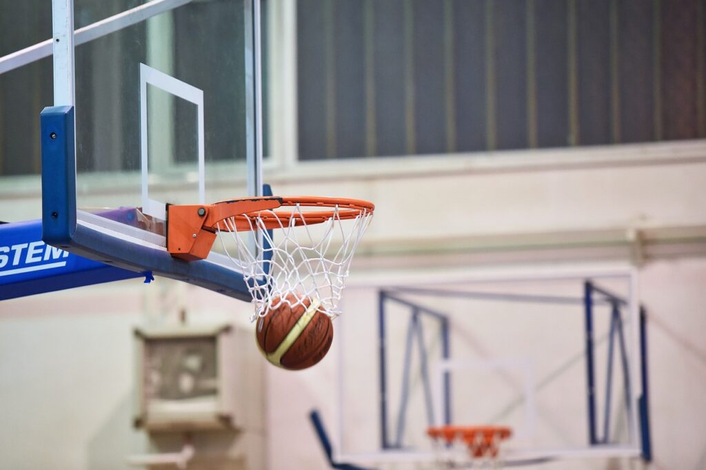 Ein Basketball, der durch einen Korb in einer Sporthalle fliegt.